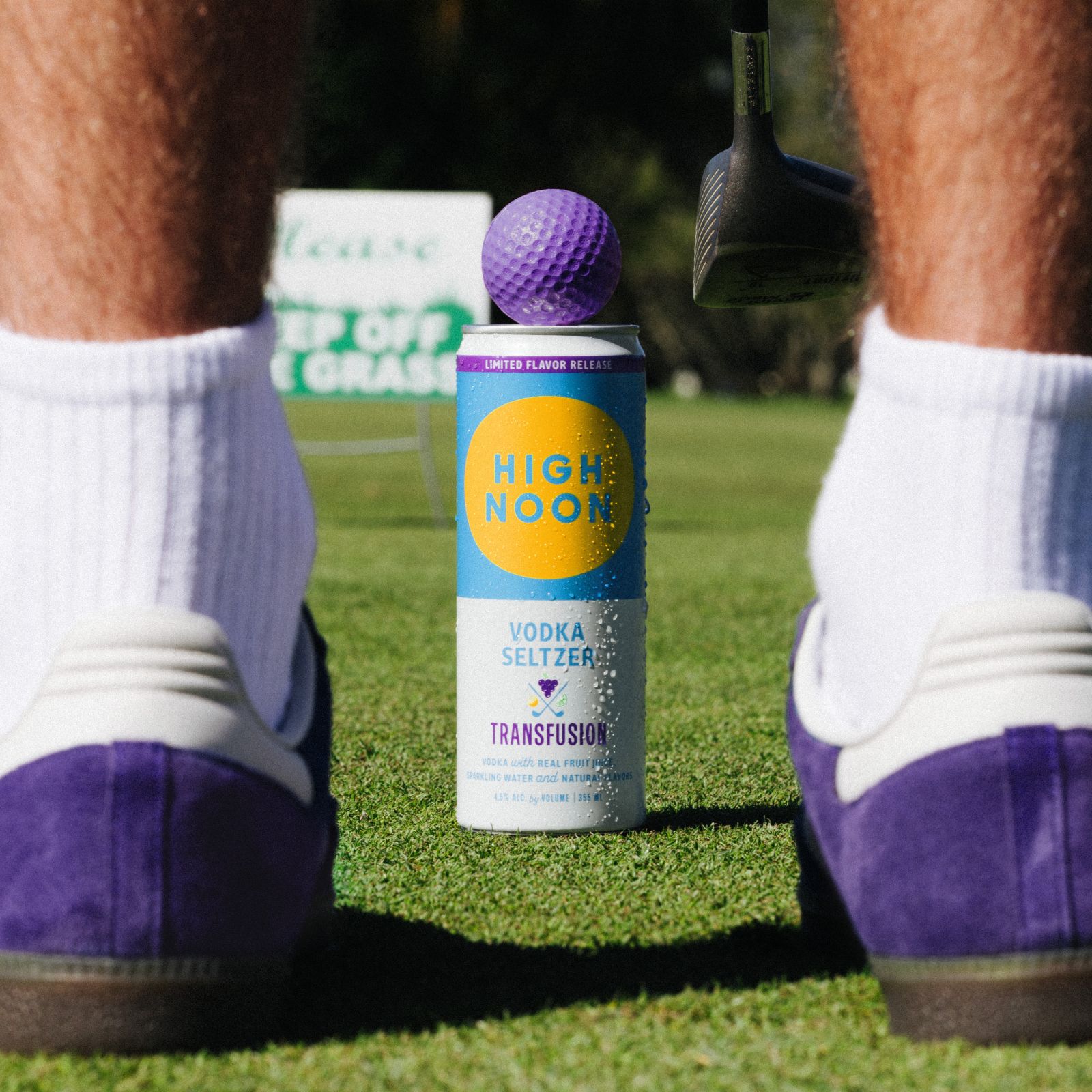 Image High Noon Transfusion can on a golf course with a golfer standing over a purple golf ball, wearing purple shoes